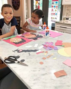 two children sitting at a kitchen table with paper cutouts on it and scissors in front of them