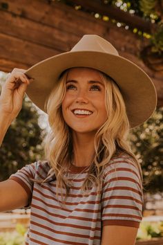 a woman wearing a hat and smiling at the camera with her hand on her hip