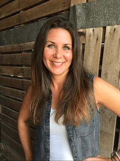 a woman standing in front of a wooden wall with her hands on her hips and smiling at the camera