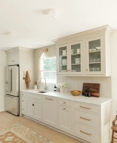 a kitchen with white cabinets and wooden flooring next to a large rug on the floor