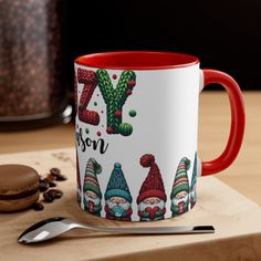 a red and white coffee mug sitting on top of a wooden table next to a cookie