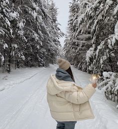 a woman walking down a snow covered road holding a sparkler in one hand and looking at the trees