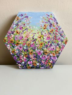 a painting of colorful flowers on a hexagonal box sitting on a white surface