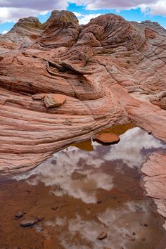 some rocks and water in the middle of a desert area with clouds reflected in it