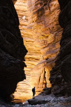 a man standing in the middle of a narrow canyon between two large rocks with sunlight streaming through them