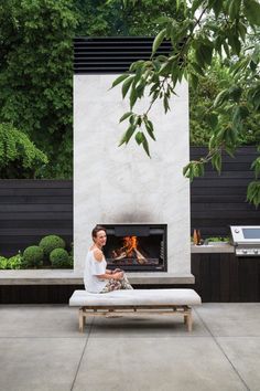 a woman sitting on a bench in front of a fire place with an outdoor fireplace