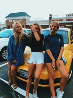 three beautiful young women standing next to a yellow car