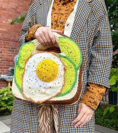 a woman is holding a crocheted bag with an egg in the center on it