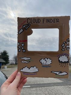 someone holding up a cardboard box with clouds on it