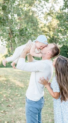 a man holding a baby up to his face while standing next to a woman in a field