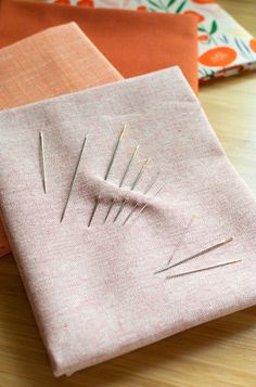 three different colored fabrics with needles sticking out of them on a wooden table next to each other