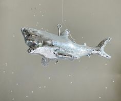 a silver ornament shaped like a shark hanging from a string on a wall