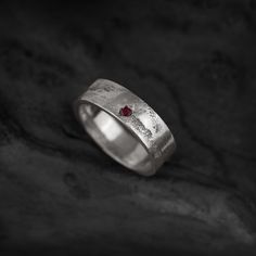 a white gold ring with a red stone in the center on a black rock surface