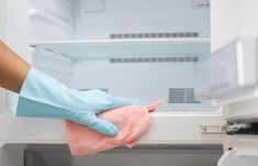 a person in blue gloves is cleaning an open refrigerator with a micro towel and rag