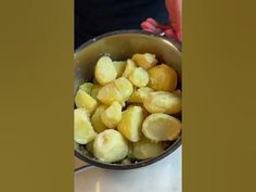 a pot filled with potatoes sitting on top of a counter next to a person's hand