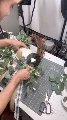 a woman is working on some flowers and greenery with scissors, tape and wire