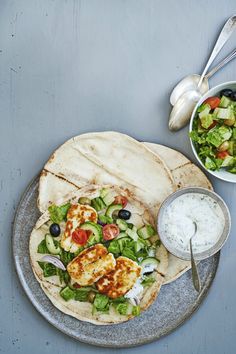 two pita breads on a plate with salad and dressing next to each other