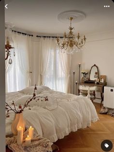 a white bed sitting in a bedroom next to a chandelier and two candles