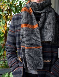 a woman wearing a gray and orange striped scarf with her hands in her pockets while standing outside