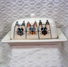 three ceramic cats sitting on top of a white plate with eyes painted on it's sides