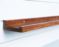 a wooden shelf mounted to the side of a white building with wood trimmings