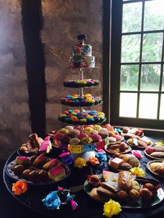 a table topped with lots of donuts and pastries on top of plates next to a window