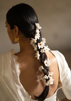 a woman with long black hair wearing a white dress and flower in her hair, looking off to the side