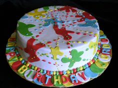 a birthday cake decorated with colorful letters and animals on the bottom layer is sitting on a black surface