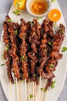 several skewers of food on a plate with oranges and dipping sauce in the background