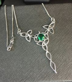 "I've designed this long, statement Celtic inspired necklace entirely in sterling silver featuring a center, faceted 10x8mm peridot gemstone! The frame, or centering, of the pendant is made with Celtic Trinity Knots and sterling wire work braids down the center to add the balancing touches to the piece. It comes with a sterling box chain which is soldered to each end of the pendant. This piece is 18\" in length, including the chain, and the pendant, itself, is approximately 3 inches, in height, Silver Peridot Jewelry As Gift, May Birthstone Jewelry In Silver With Peridot, Silver Peridot Jewelry For May Birthstone, Silver Peridot Jewelry With Gemstone, Silver Peridot Jewelry For Anniversary, Sterling Silver Green Jewelry With Jewels, Silver Peridot Birthstone Jewelry, Green Sterling Silver Jewelry With Jewels, Silver Emerald Jeweled Necklace For Anniversary