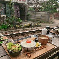 a wooden table topped with bowls of food next to a rail road track and train tracks