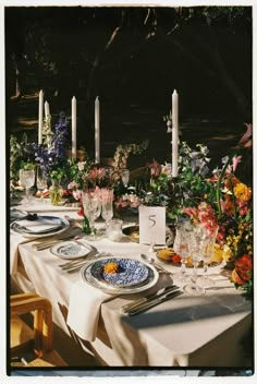 the table is set with flowers and candles for an outdoor dinner party or gathering in the garden