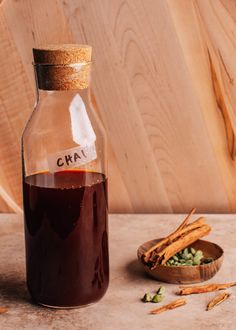 a glass bottle filled with liquid next to some cinnamon sticks and other spices on a table