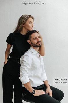 a man and woman sitting on top of each other in front of a white wall