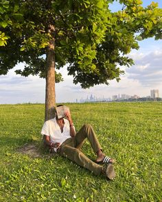 a man sitting under a tree talking on a cell phone while holding his head in his hands