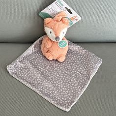 a small stuffed animal sitting on top of a gray blanket next to a couch cushion