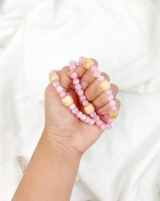 a hand holding some pink beads on it's fingers and wearing a bracelet with wooden beads