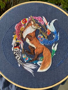 a person is holding up a hand embroidered picture with an image of a fox and fish on it