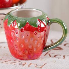 a red and green glass mug sitting on top of a table next to some apples