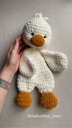 a crocheted teddy bear is being held by a woman's hand on a gray surface