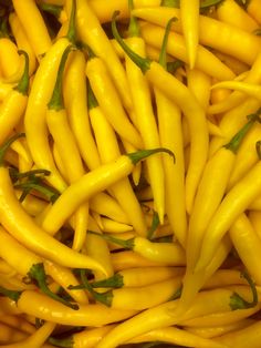 yellow peppers with green leaves on them are piled together in a large pile and ready to be eaten