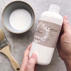 a person holding a bottle of liquid next to a bowl and brush