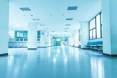 an empty hospital hallway with blue chairs and large windows on either side of the room