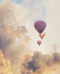 two hot air balloons flying in the sky with clouds behind them and one is pink