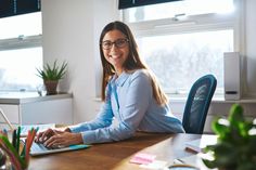 a woman sitting at a desk with a laptop computer in front of her, smiling