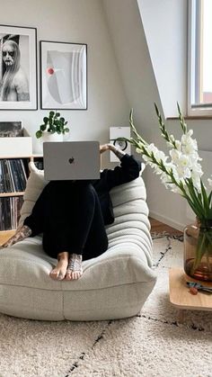 a woman sitting on top of a couch using a laptop computer next to a vase with flowers