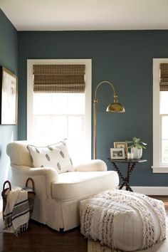 a living room with blue walls and white furniture in the corner, along with two windows