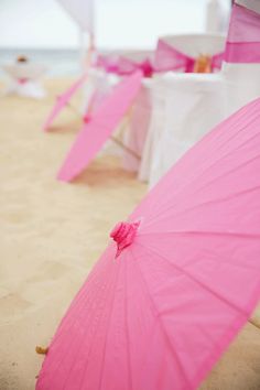 pink umbrellas are lined up on the beach for an outdoor wedding ceremony at the ocean