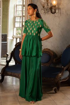 Emerald green chiniya silk padded peplum with antique tone gold sequins and zari embroidery in floral patterns. Comes with cotton silk base palazzo.
Components: 2
Pattern: Embroidered
Type Of Work: Floral
Neckline: Round
Sleeve Type: Short
Fabric: Peplum : Chiniya silk, Palazzo : Cotton silk
Color: Emerald Green
Other Details: 
Peplum:
Padded
Floral buttis
Attached lining top yoke
Palazzo:
Attached lining
Karigari time: 50 hrs
Occasion: Destination Wedding - Aza Fashions Paulmi And Harsh, Cotton Palazzo Pants, 1950’s Fashion, Zari Embroidery, Dress And Jacket Set, Palazzo Set, Indian Clothes, Gold Sequins, India Fashion