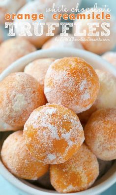 powdered sugar coated donuts in a white bowl on a blue tablecloth with other doughnuts